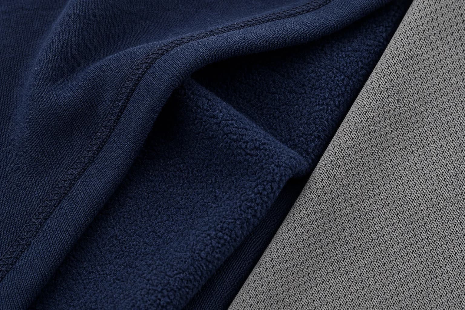 Macrofoto van zware navy fleece stof naast een grijze technische knit met zichtbare vezelstructuur
